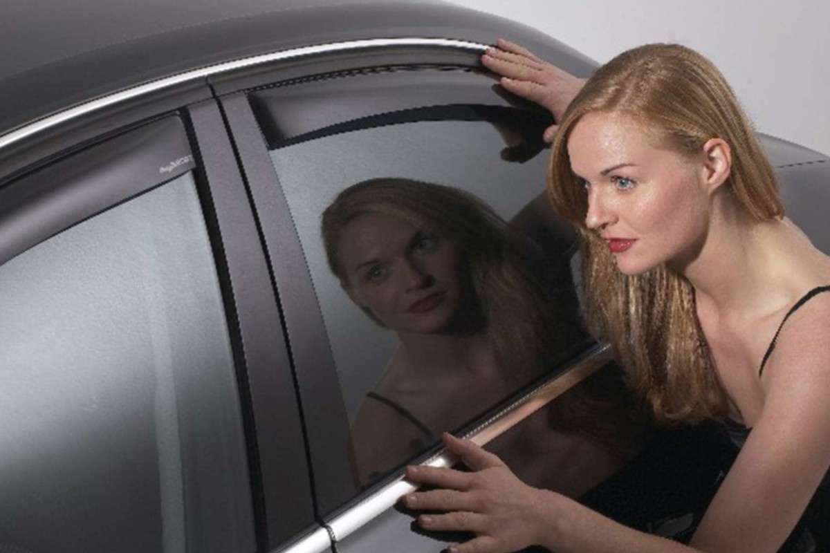 eine Frau betrachtet die Windabweiser an einem Auto