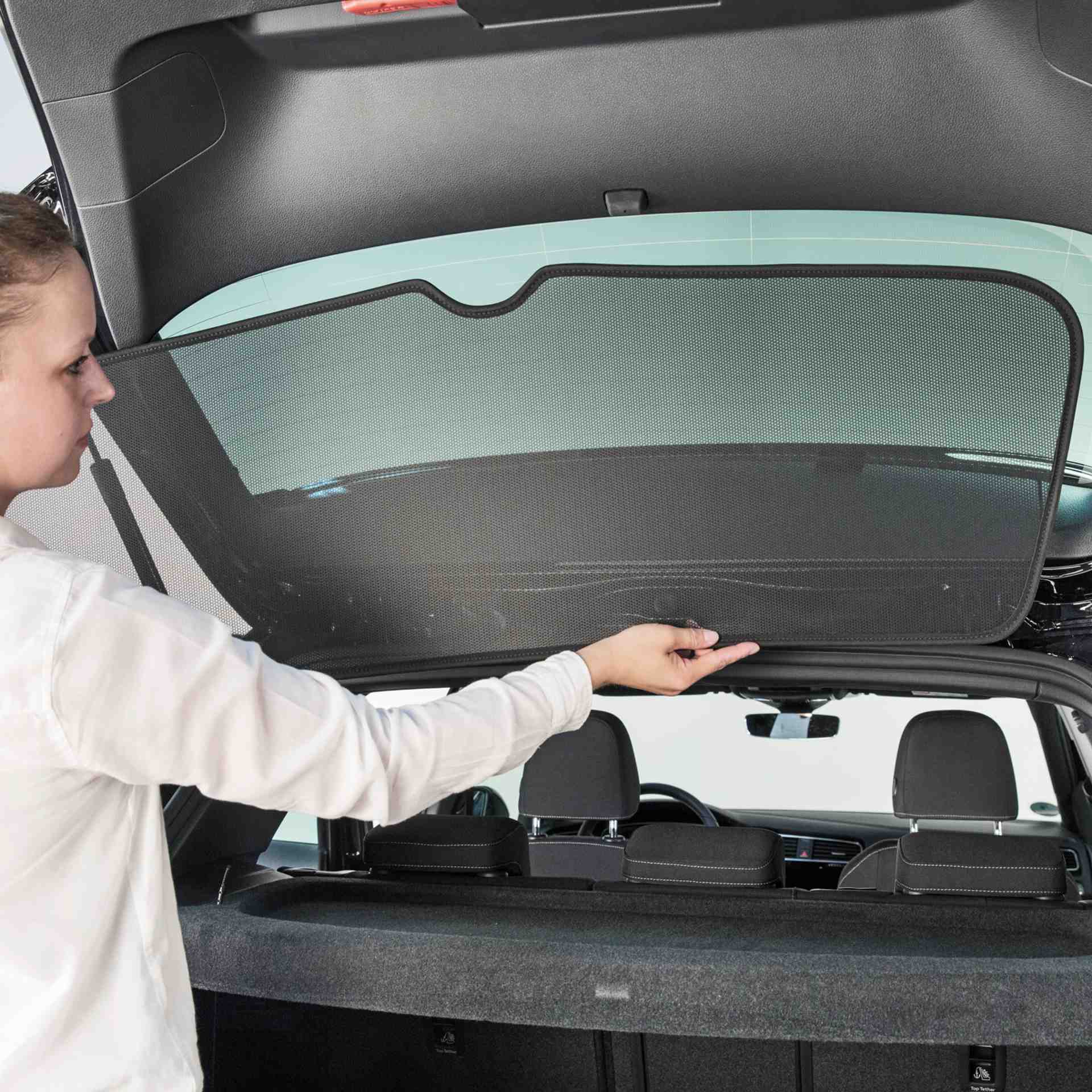 eine Frau bringt den Sonniboy an die Heckscheibe eines Autos an