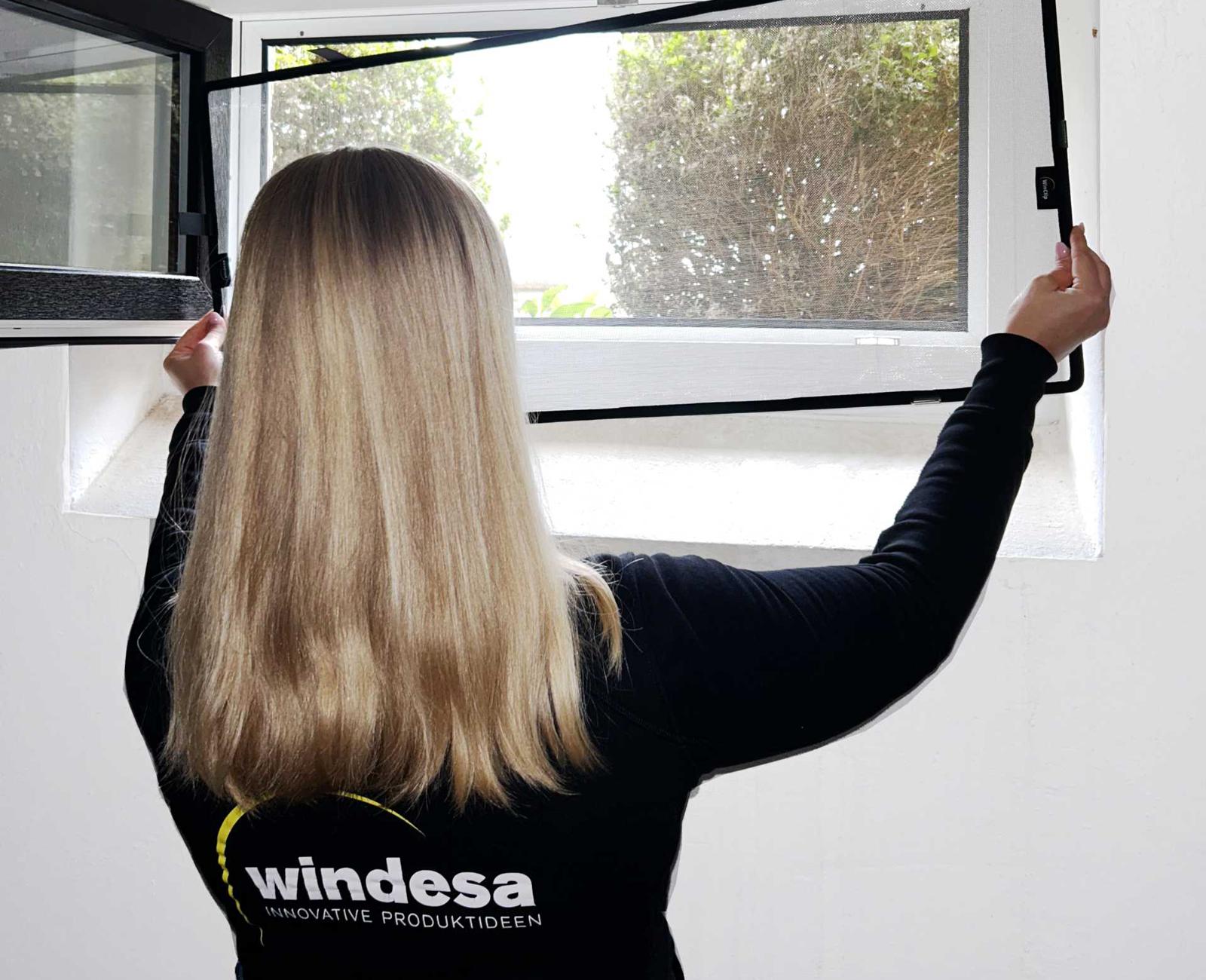 eine Frau hält einen Nageschutz an ein Kellerfenster