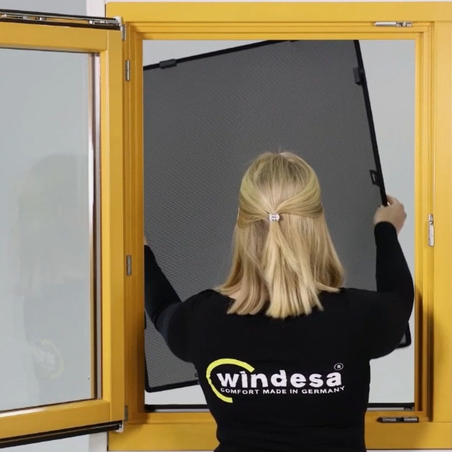 A woman installs the WinClip Multi in a wooden window
